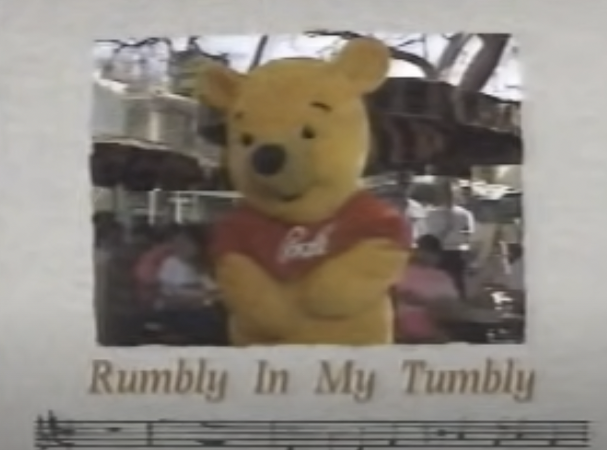 "Winnie the Pooh holds his tummy against a paper background with sheet music titled 'Rumbly In My Tumbly'"